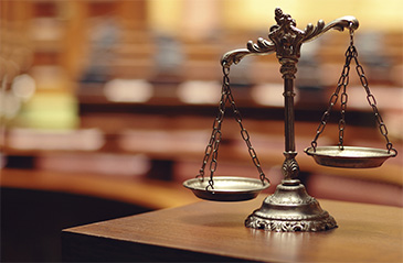 Scales of Justice on wooden table, courtroom blurred in the background